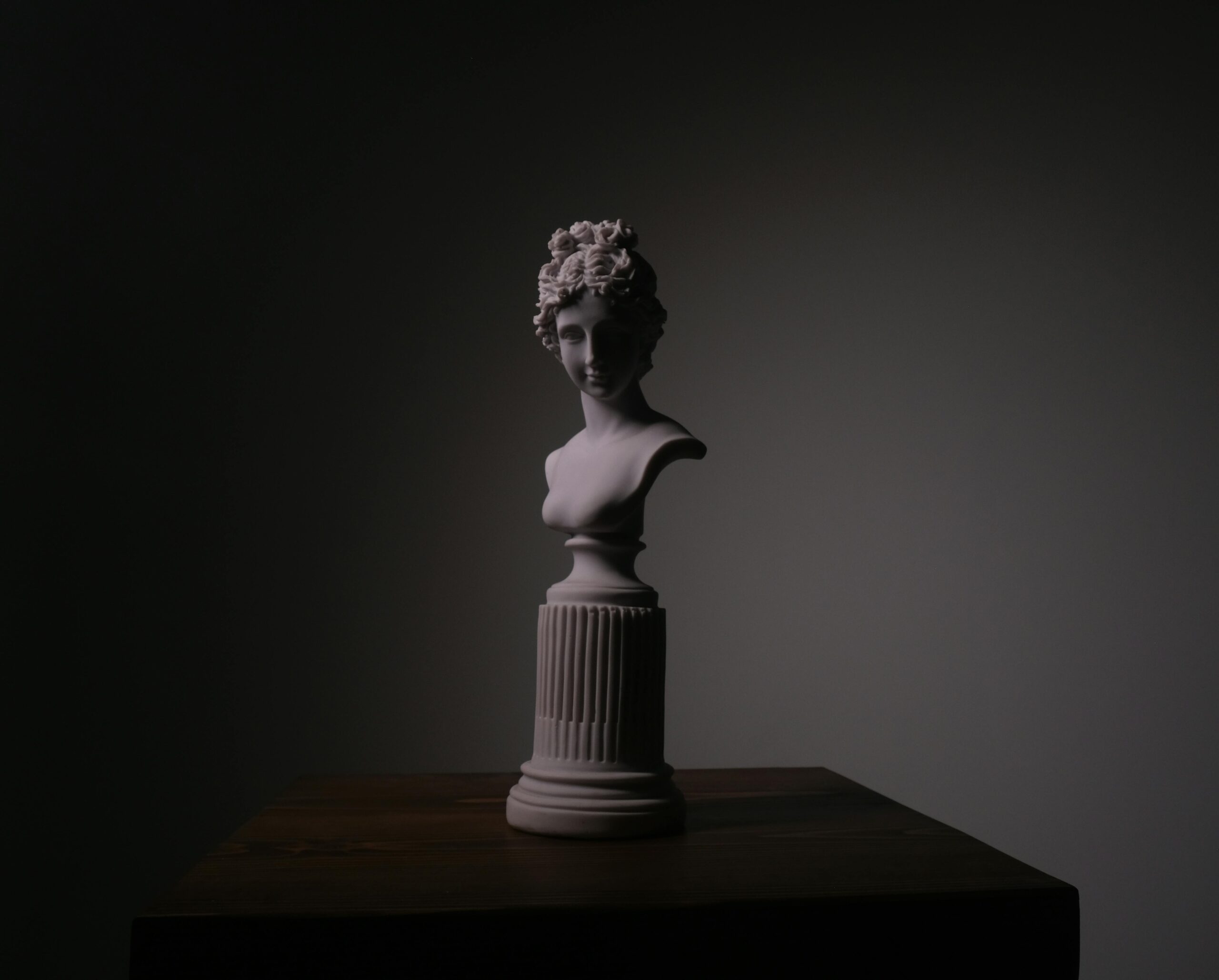 Elegant classical sculpture bust on a pedestal with dramatic lighting in a studio setting.