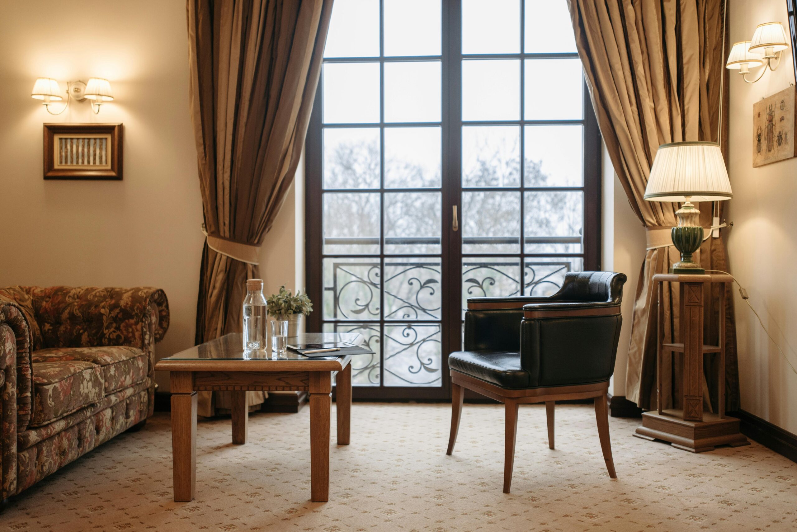 Stylish living room featuring a classic armchair, sofa, wooden table, and large window for natural light.